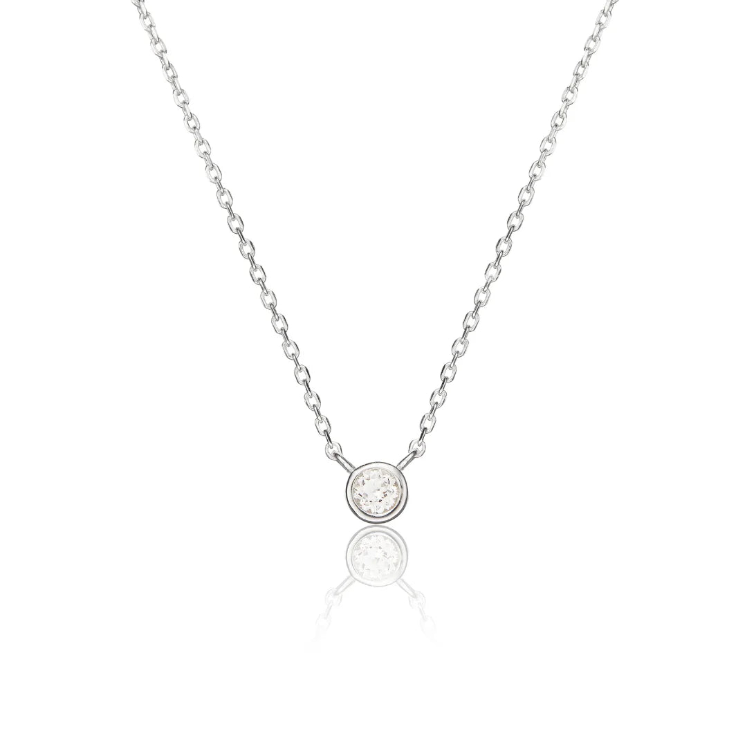 A delicate silver chain necklace with a small round bezel-set clear gemstone pendant, displayed on a clean white background with a soft reflection below.