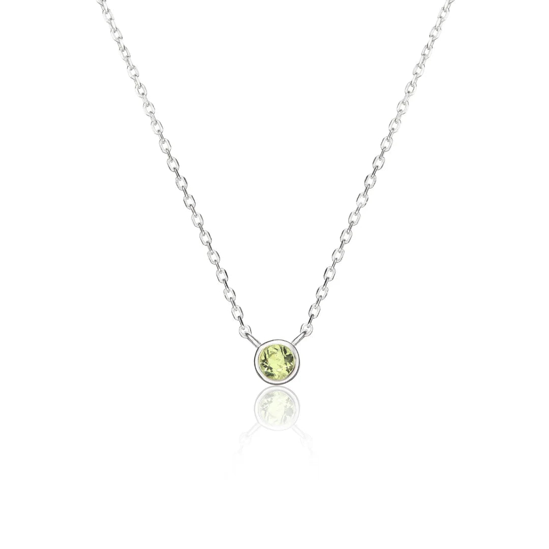A delicate silver chain necklace with a small round bezel-set clear gemstone pendant, displayed on a clean white background with a soft reflection below.