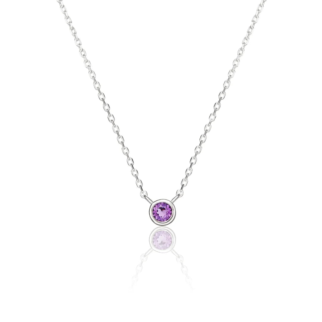 A delicate silver chain necklace with a single bezel-set round purple gemstone pendant, displayed on a clean white background with a soft reflection below.