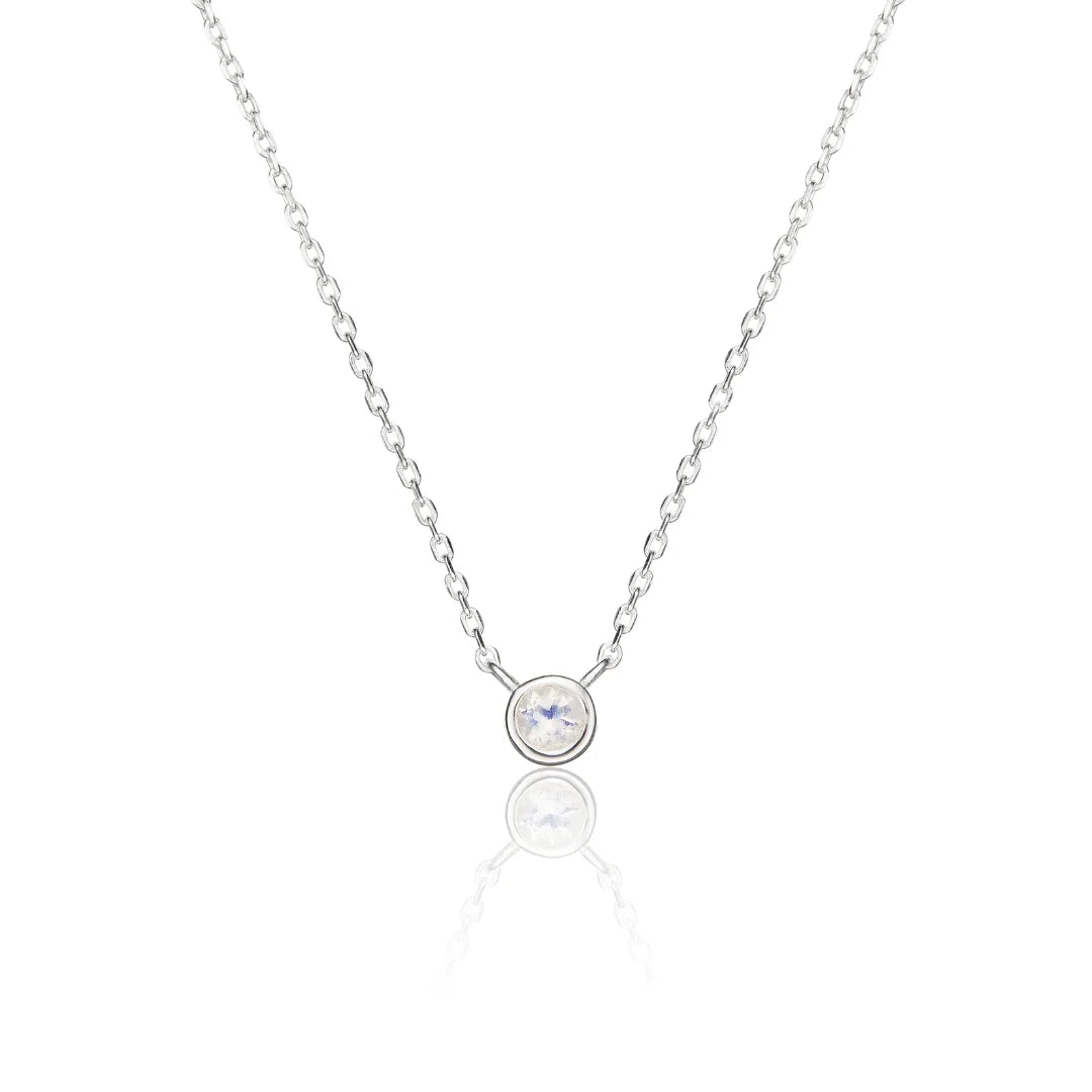 A delicate silver chain necklace with a single bezel-set round clear gemstone pendant, displayed on a clean white background with a soft reflection below.