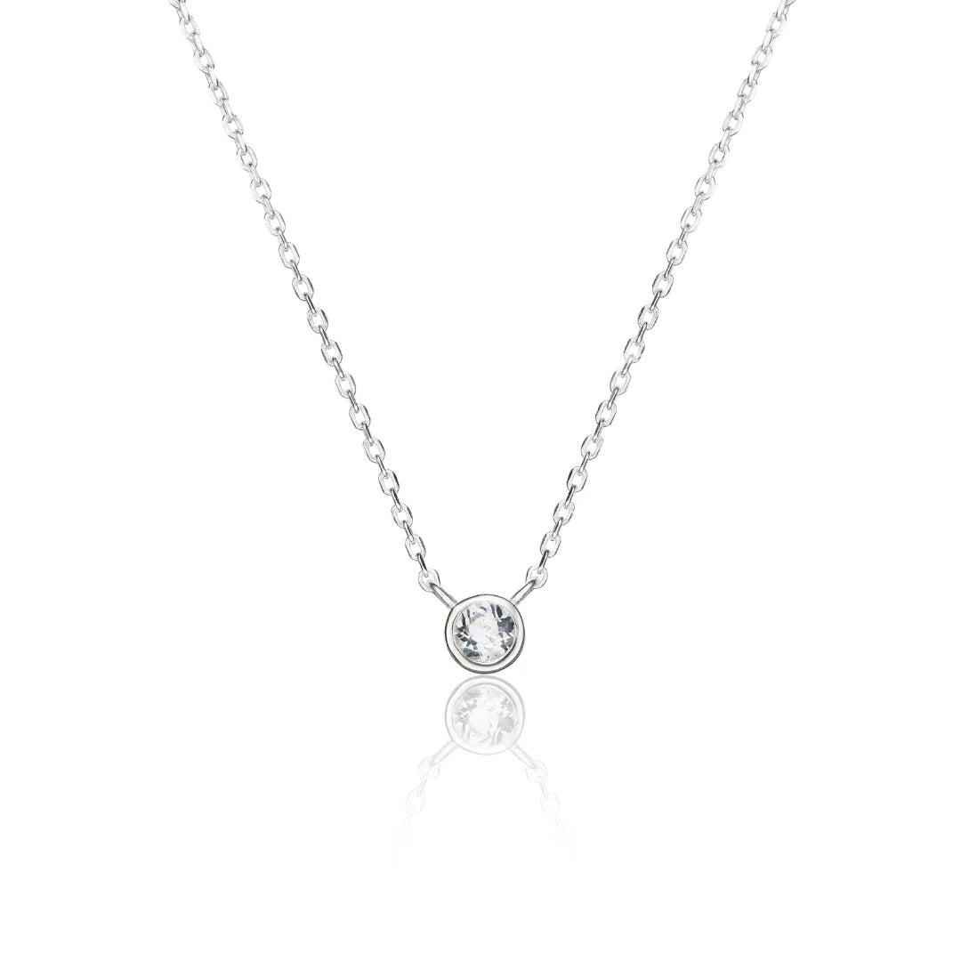 A delicate silver chain necklace with a single bezel-set clear gemstone pendant, displayed on a clean white background with a soft reflection below.