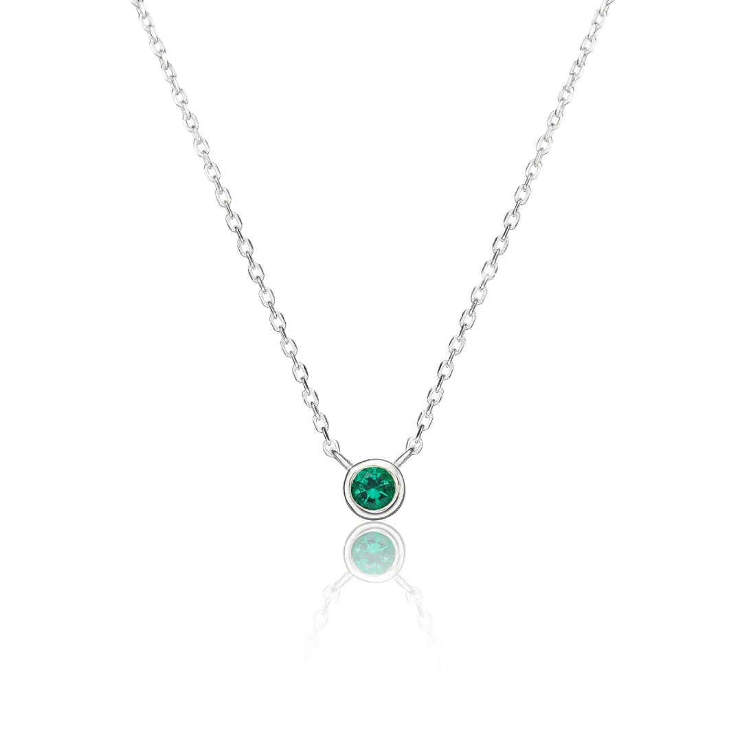 A delicate silver chain necklace with a single bezel-set round green gemstone pendant, displayed on a clean white background with a soft reflection below.