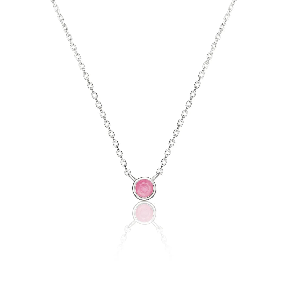A delicate silver chain necklace featuring a small round bezel-set pink gemstone pendant, displayed on a clean white background with a soft reflection below.
