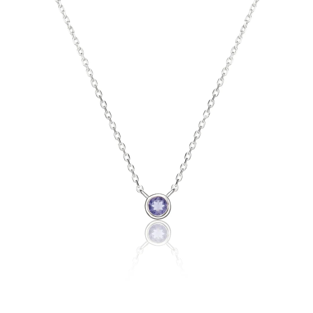 A delicate silver chain necklace with a small bezel-set round pendant featuring a light purple gemstone, displayed on a clean white background with a soft reflection below.