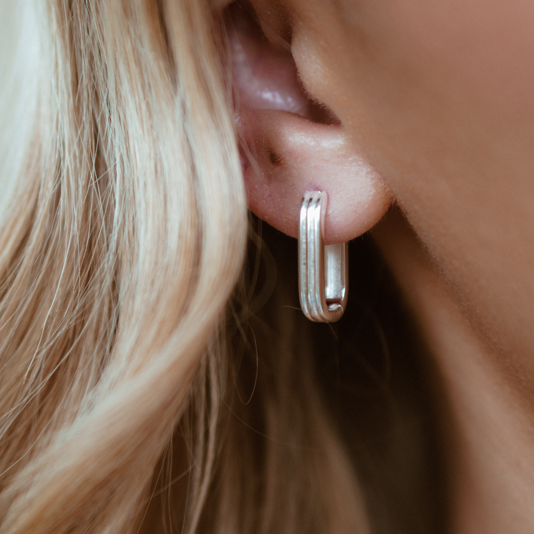 Gold ribbed pearl drop hoop earring without the pearl in an ear lobe of a blonde woman 