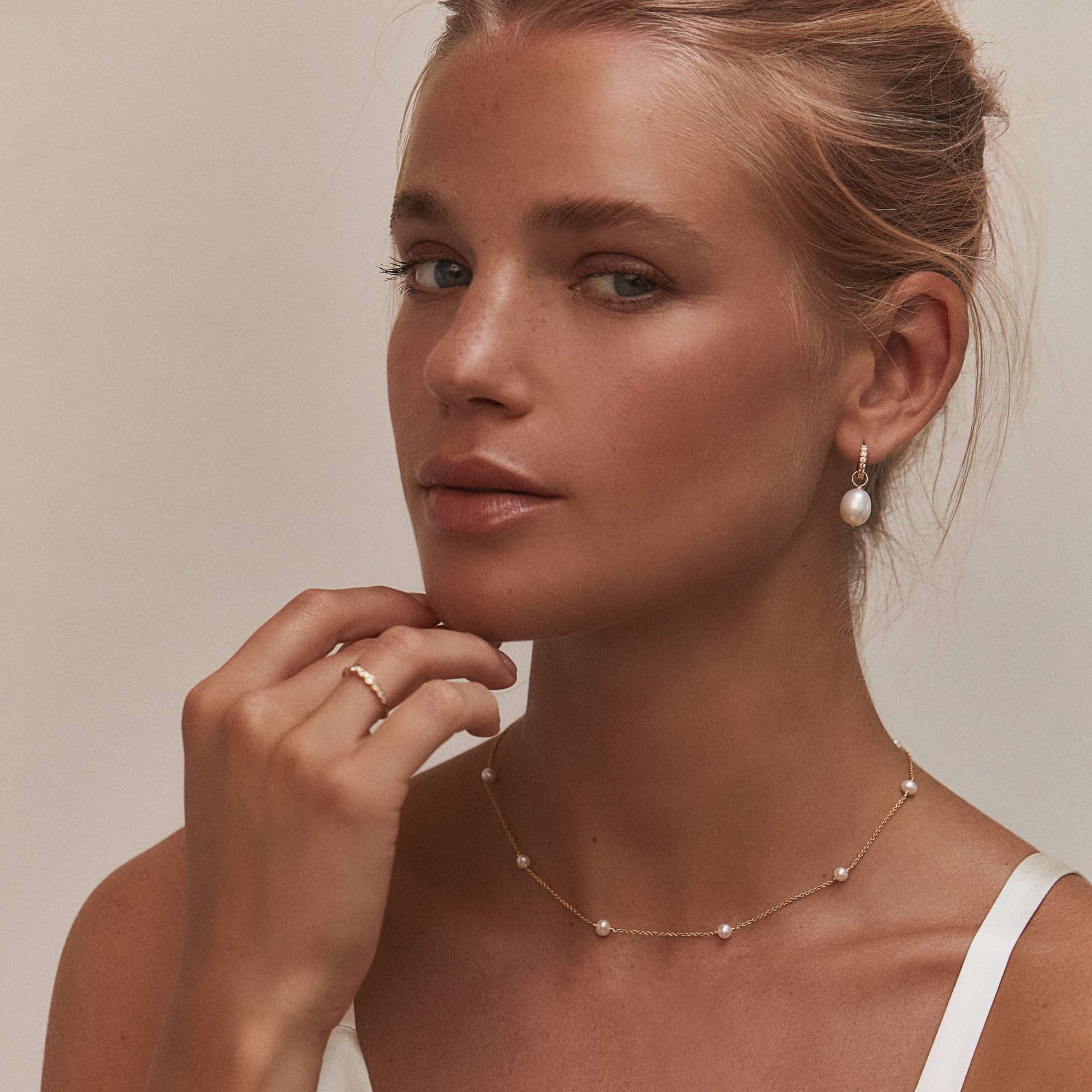 Gold huggie pearl drop earring in one ear lobe of a blonde woman wearing a pearl necklace