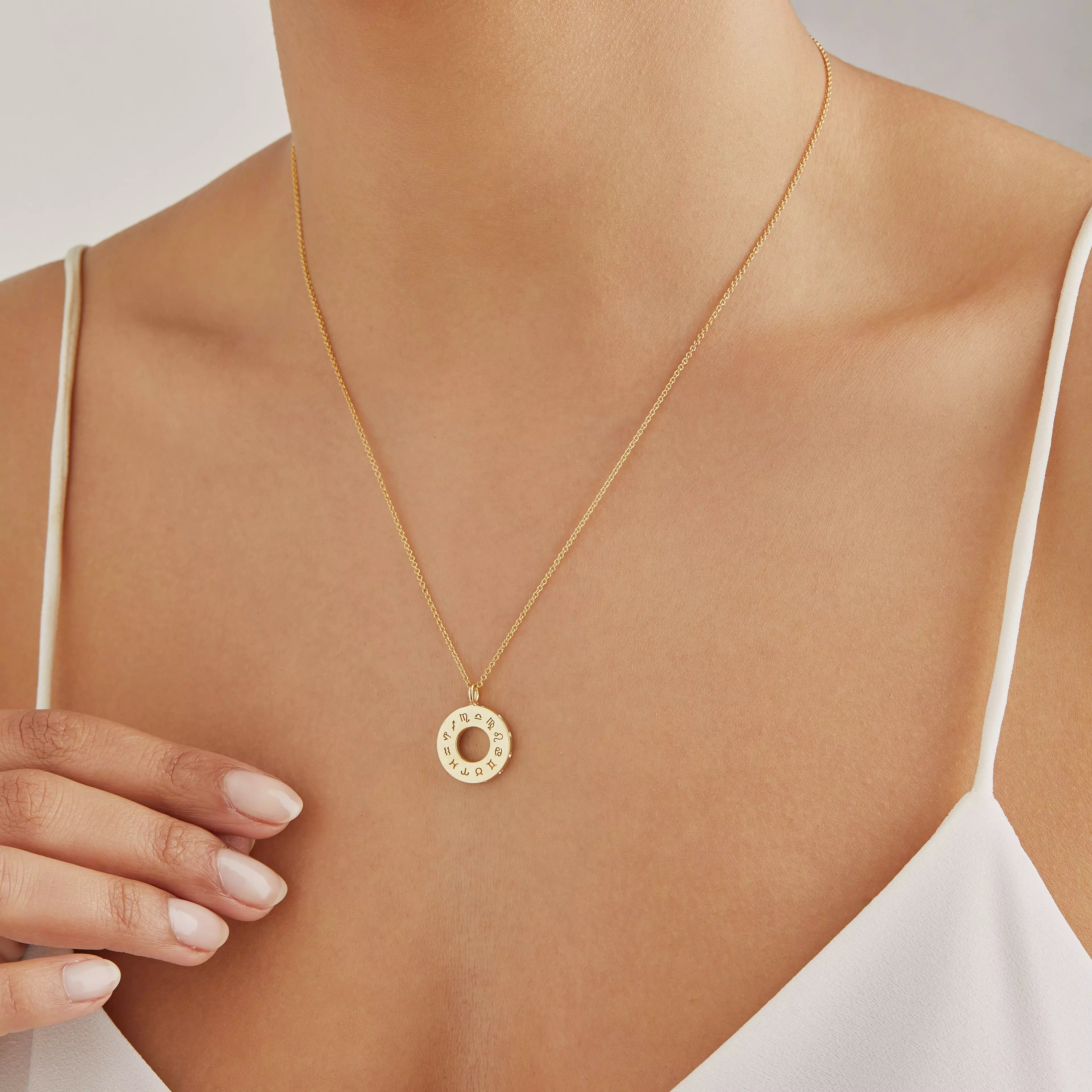 Gold zodiac birthstone necklace around a neck of a woman wearing a white strappy top