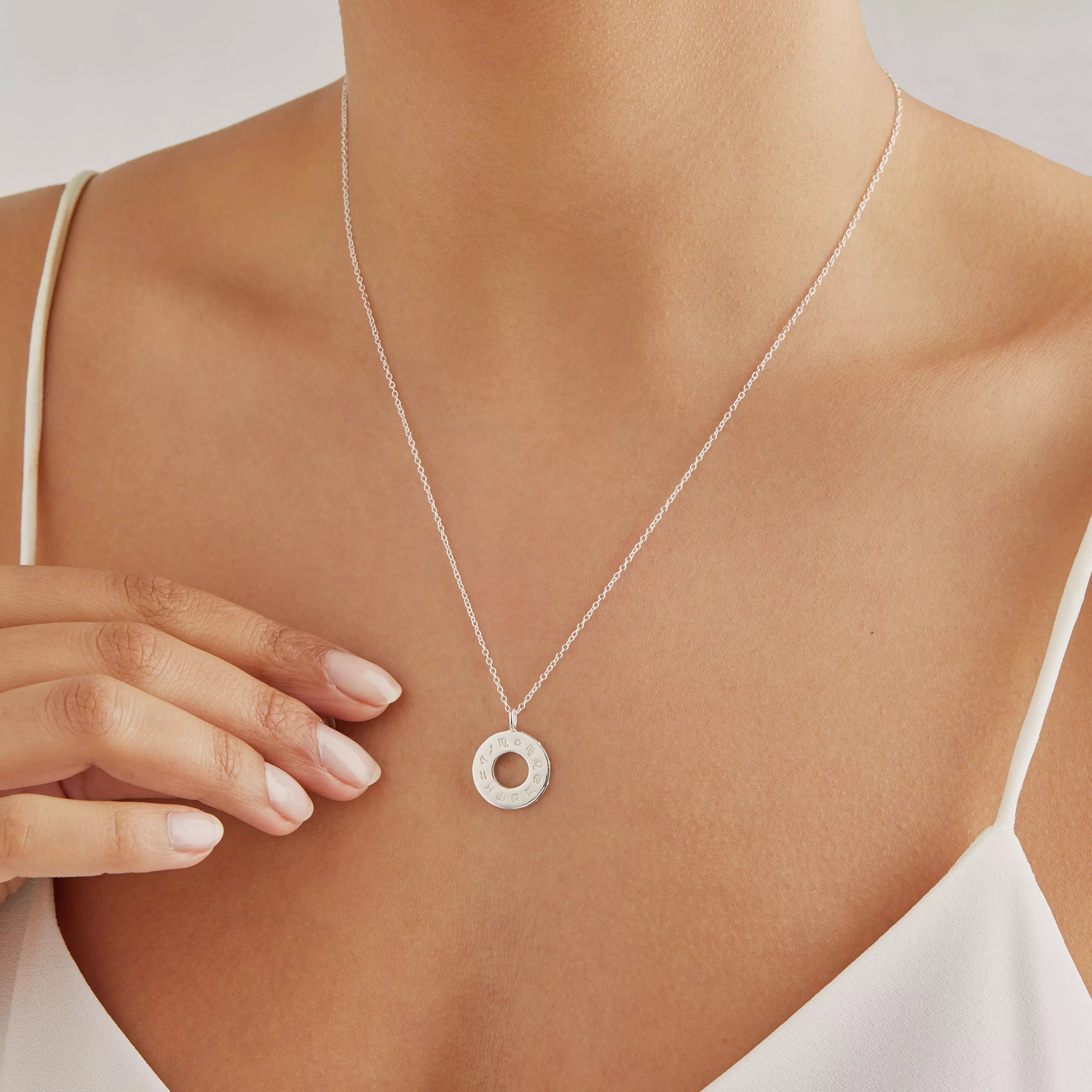 Silver zodiac birthstone necklace around the neck of a woman wearing a white strappy top