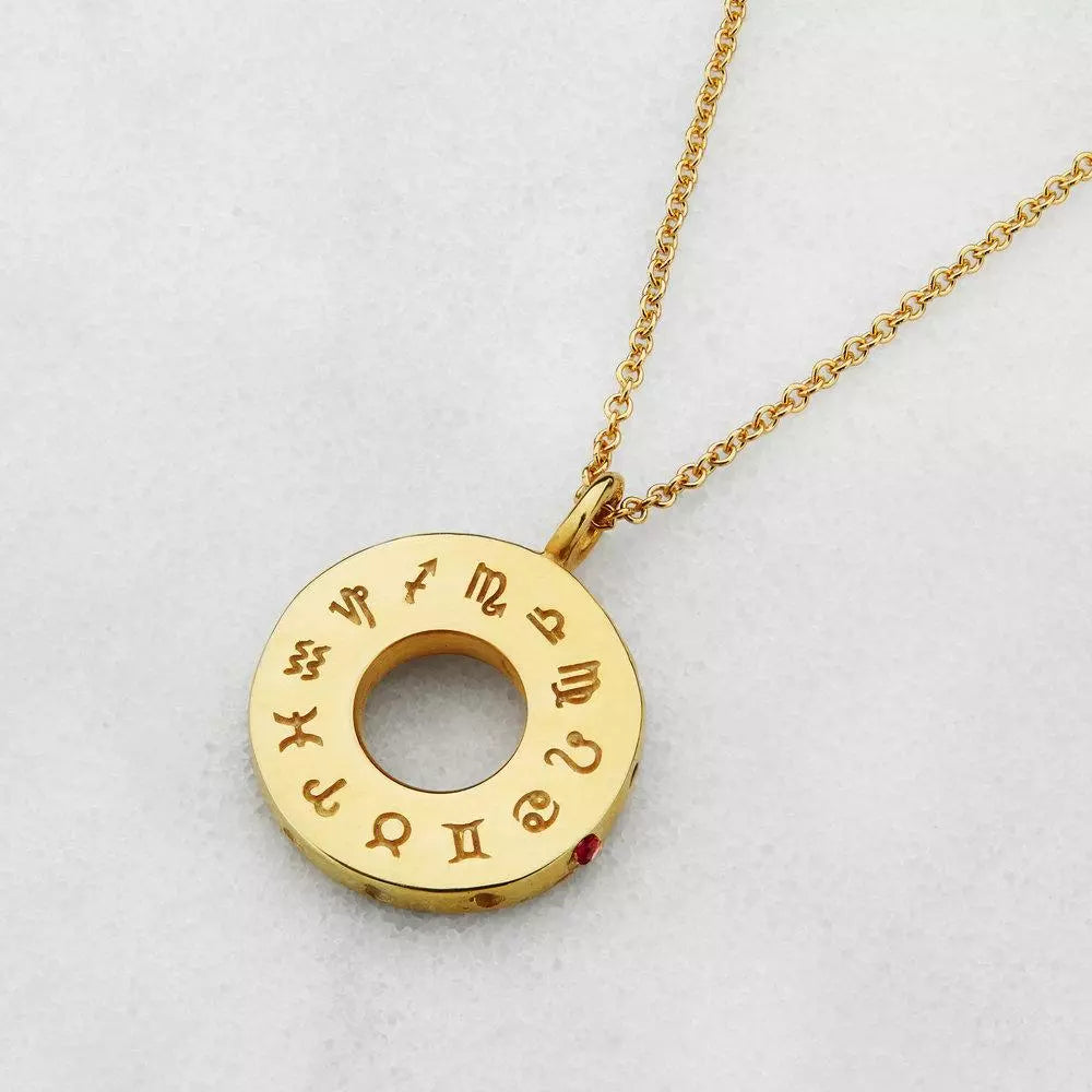 Gold zodiac birthstone necklace on a cream textured surface