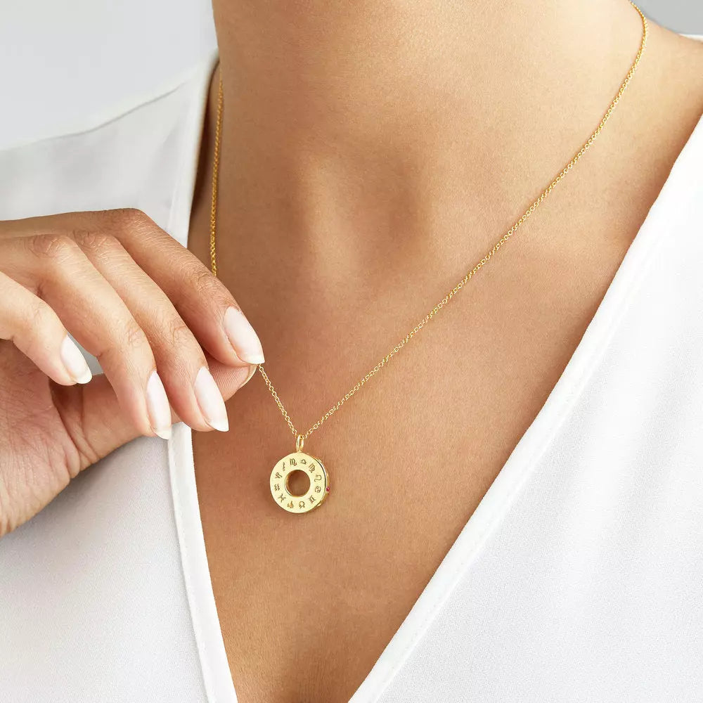 Gold zodiac birthstone necklace around the neck of a woman wearing a white V neck top