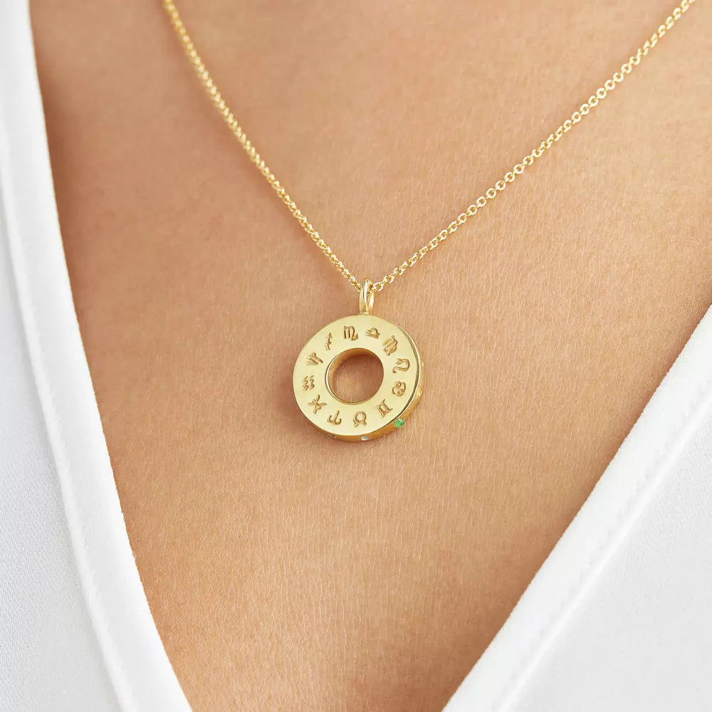 Close up of gold zodiac birthstone necklace around the neck of a woman wearing a white V neck top