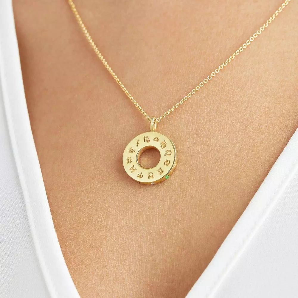 Close up of a gold zodiac birthstone necklace on a chest of a woman wearing a white V neck top