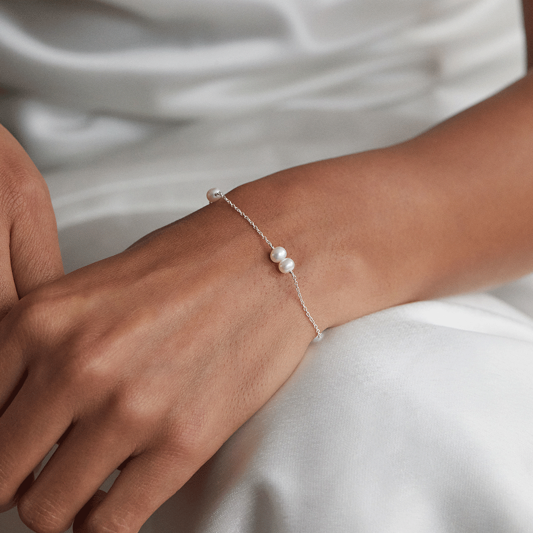 Close up of a silver six pearl bracelet around the wrist of a woman wearing white