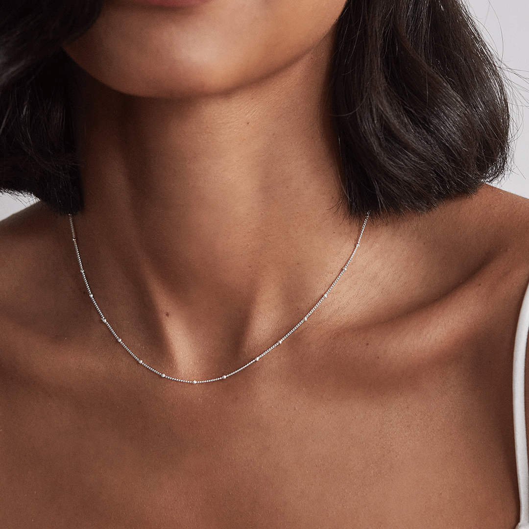 Silver satellite chain necklace around a neck of a woman with a shoulder-length hair cut