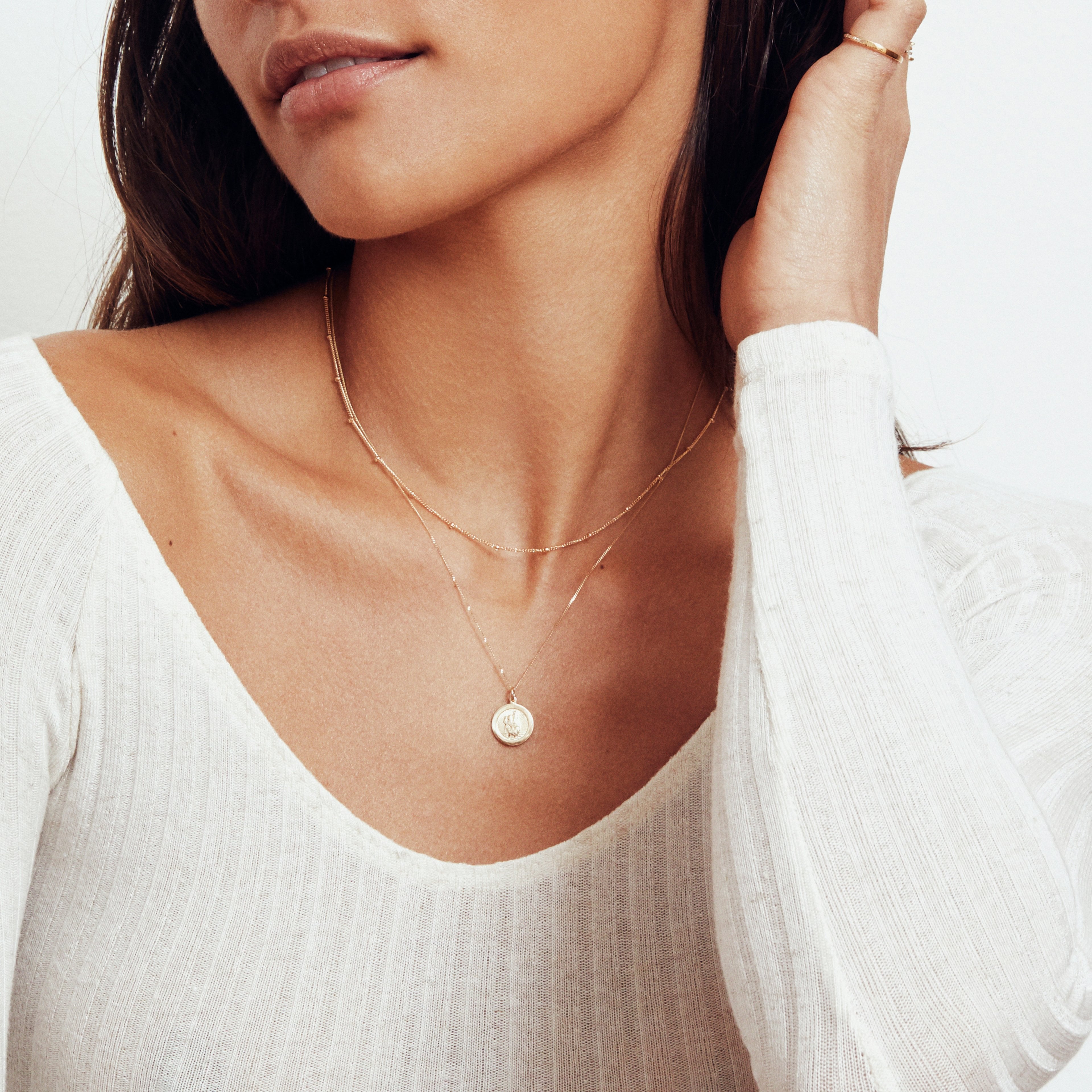 Brunette woman wearing a gold satellite chain necklace layered with with a circular gold pendant necklace around her neck