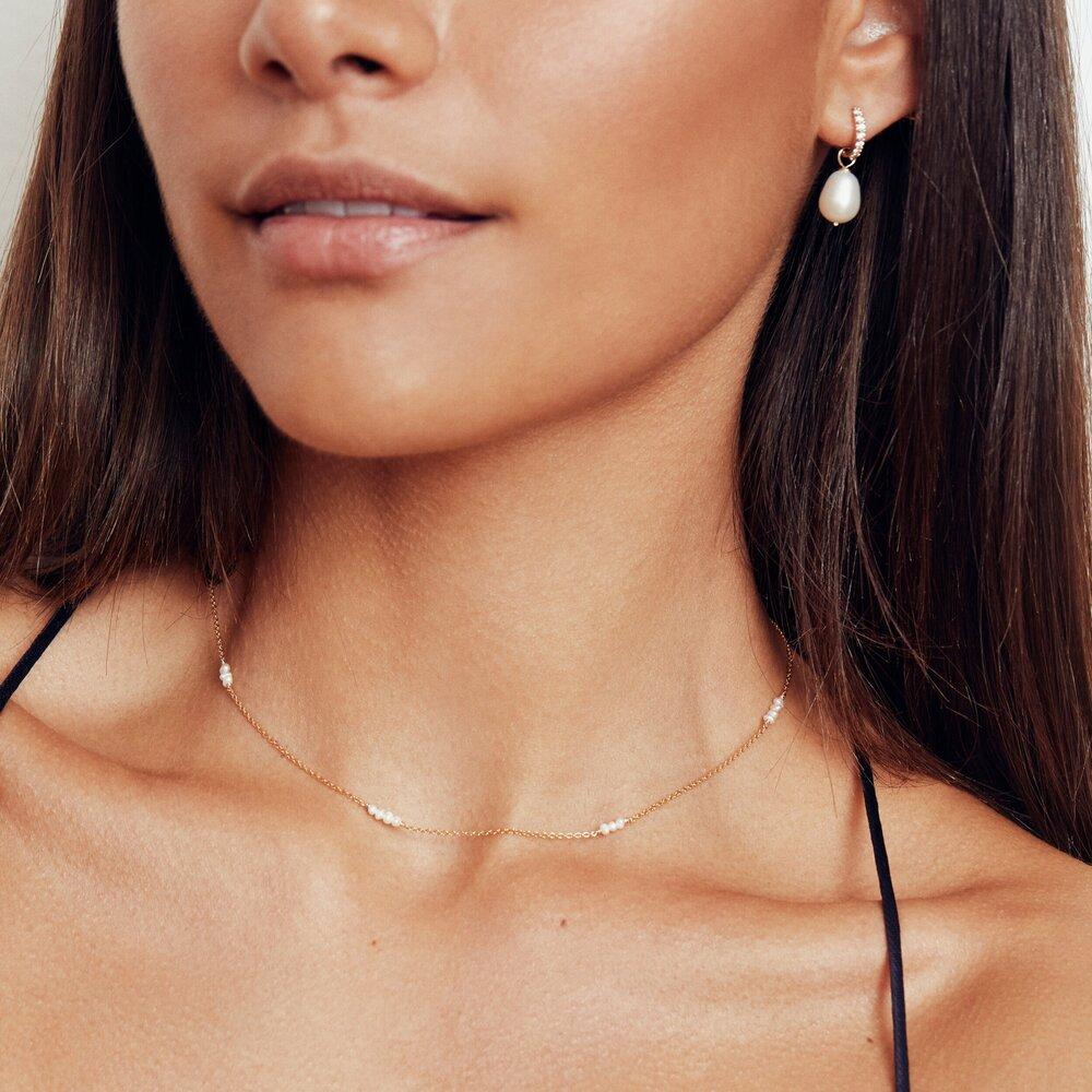 Gold mini pearl choker around a brunette woman's neck with a gold diamond style large pearl drop hoop earring in one ear lobe