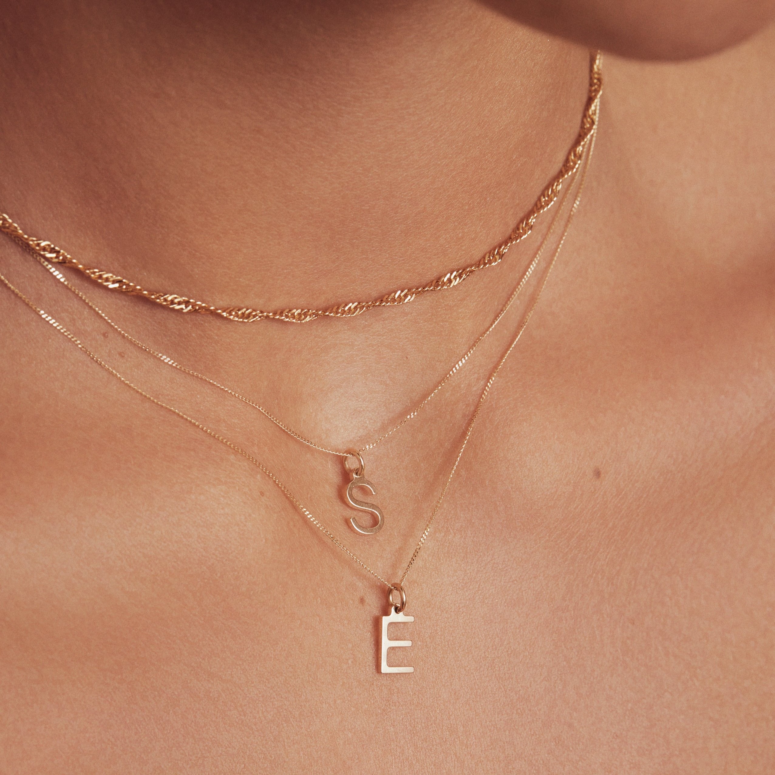 Gold twisted rope chain necklace layered with two gold chains with solid gold individual initial charms 'E' and 'S'
