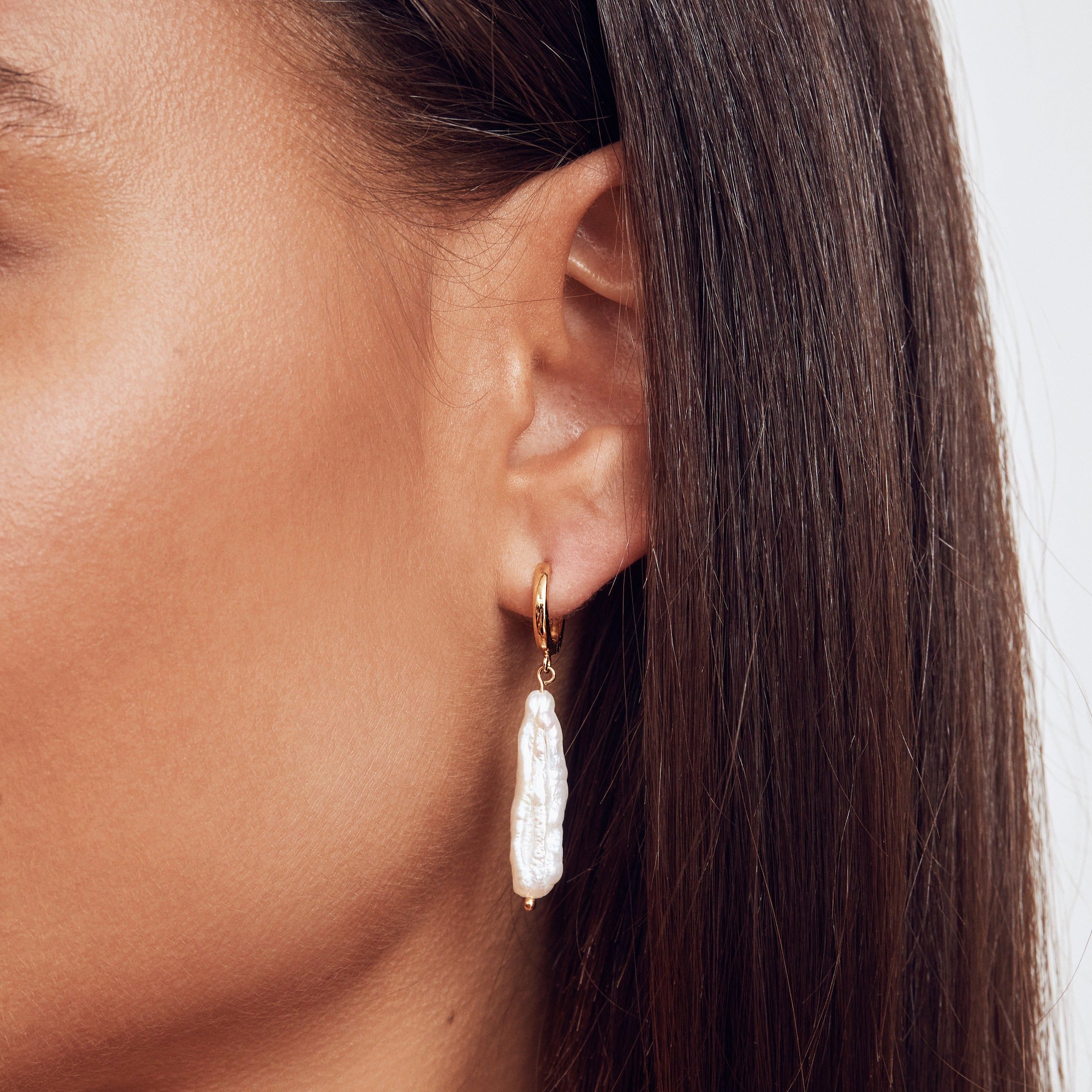 gold baroque pearl shard hoop earring in one ear lobe of a brunette woman 