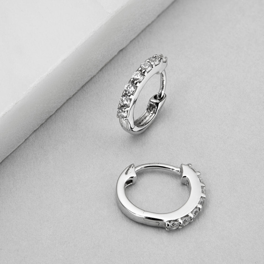 Silver diamond style huggie hoop earrings on a marble surface