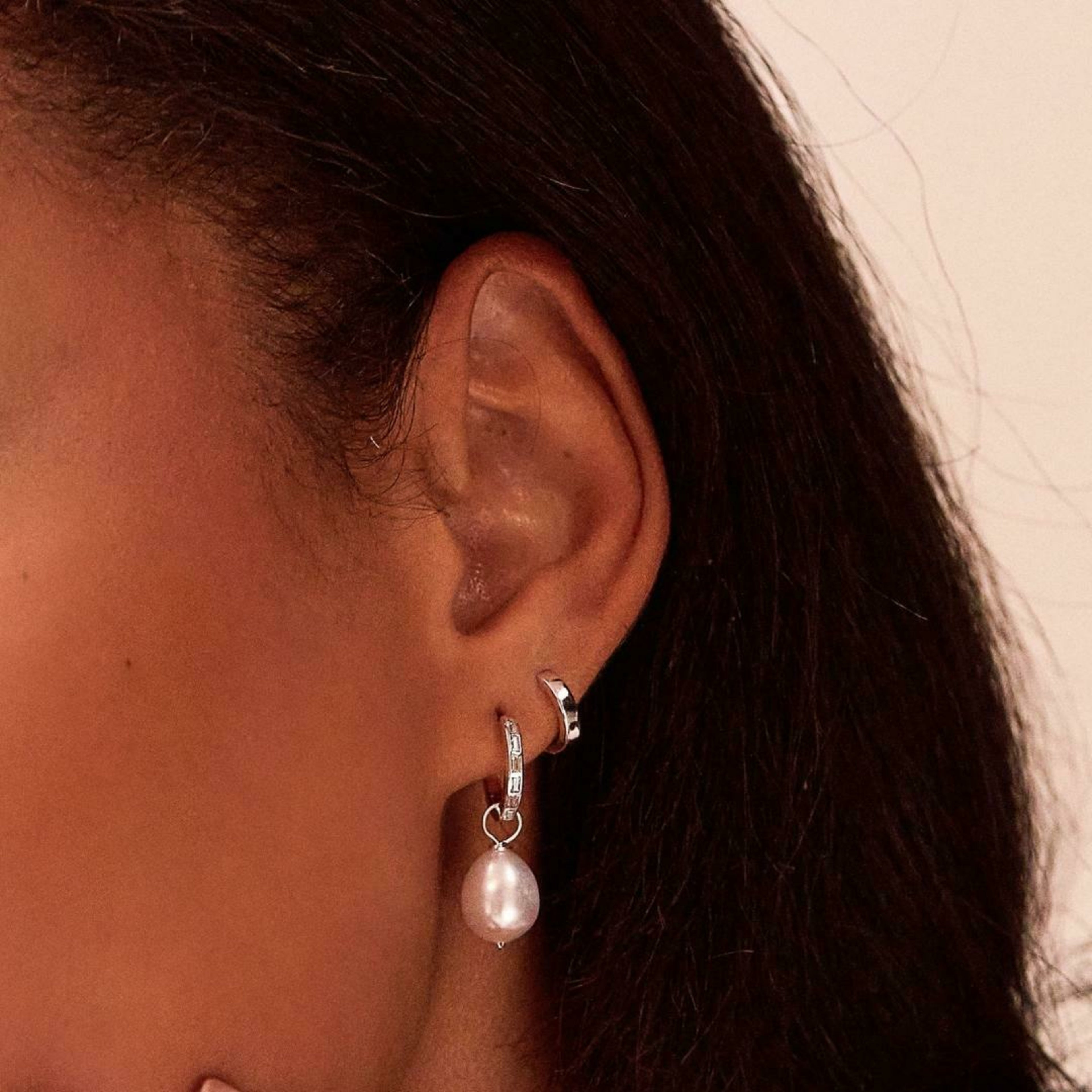 a silver diamond style baguette pearl drop hoop earring and a silver cuff in one ear lobe