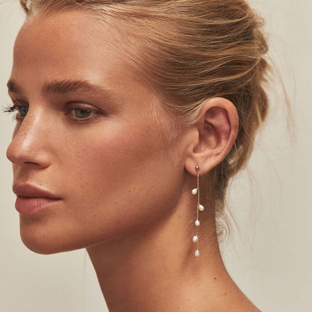 Gold seed pearl drop earring in an ear lobe of a blonde woman with her hair tied back