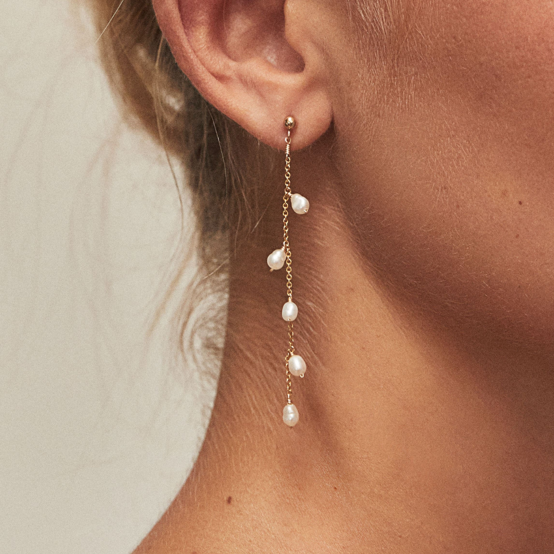 Gold seed pearl drop earring in one ear lobe close up
