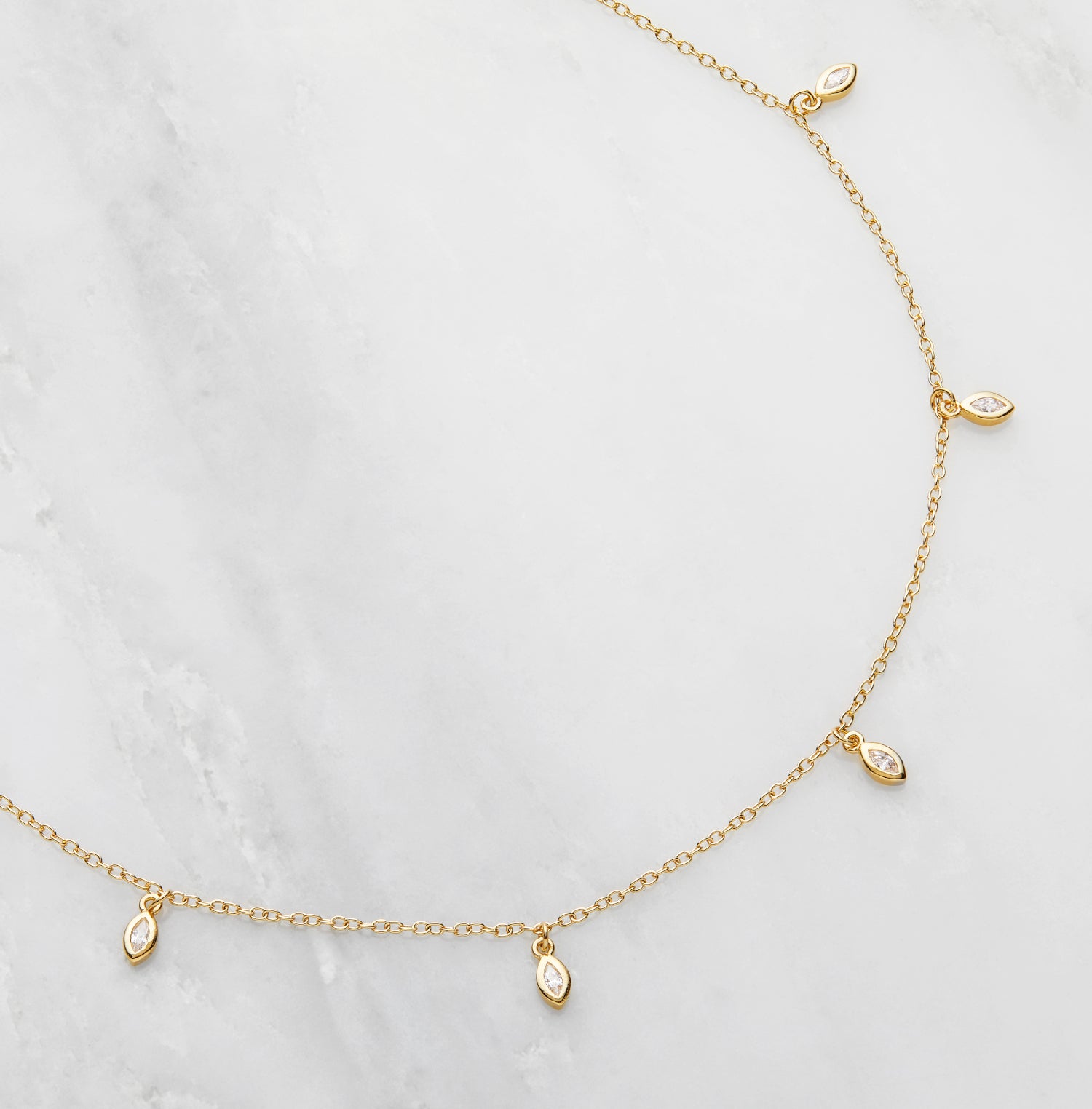 Gold diamond style marquise drop necklace on a marble surface