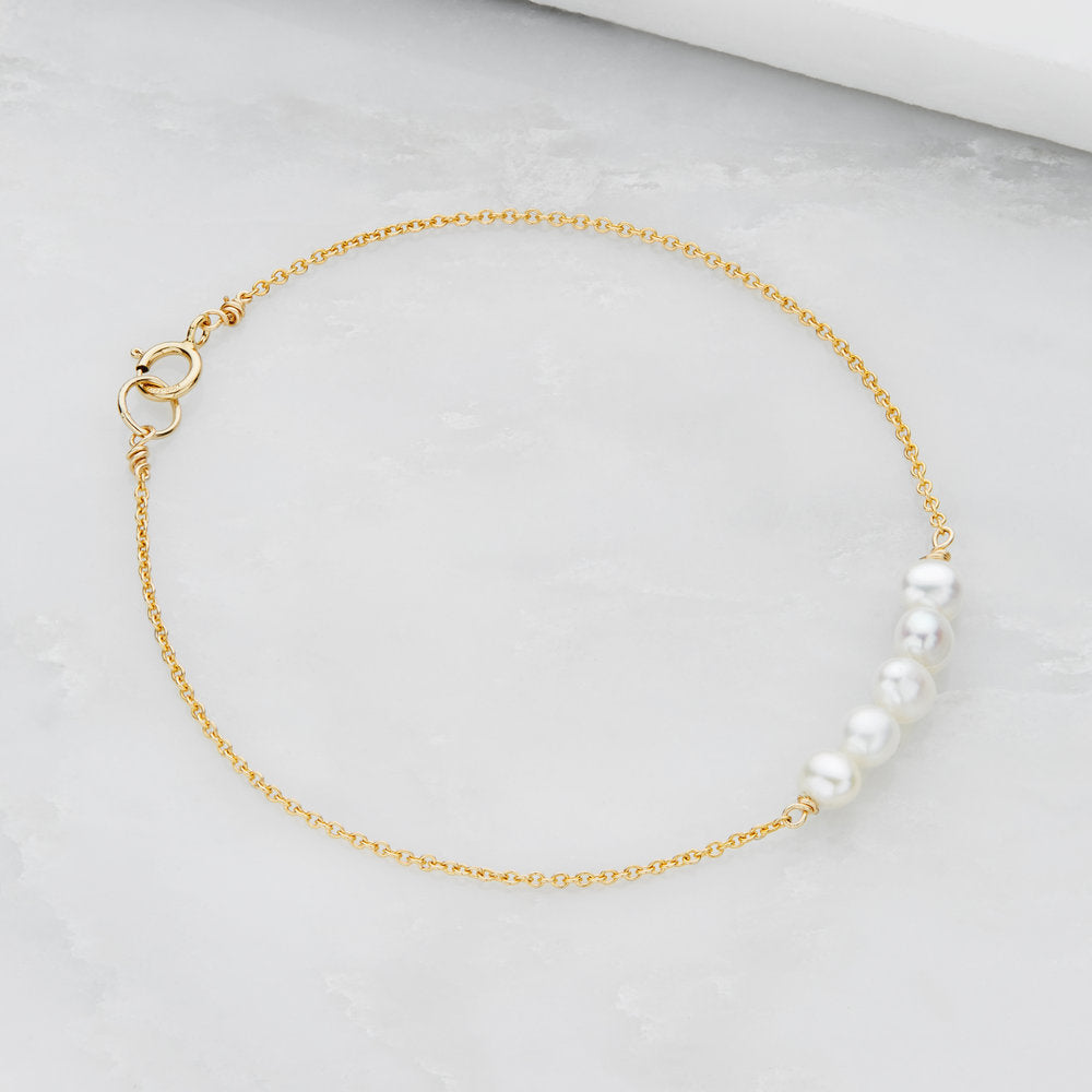 A gold cluster pearl bracelet on a marble surface