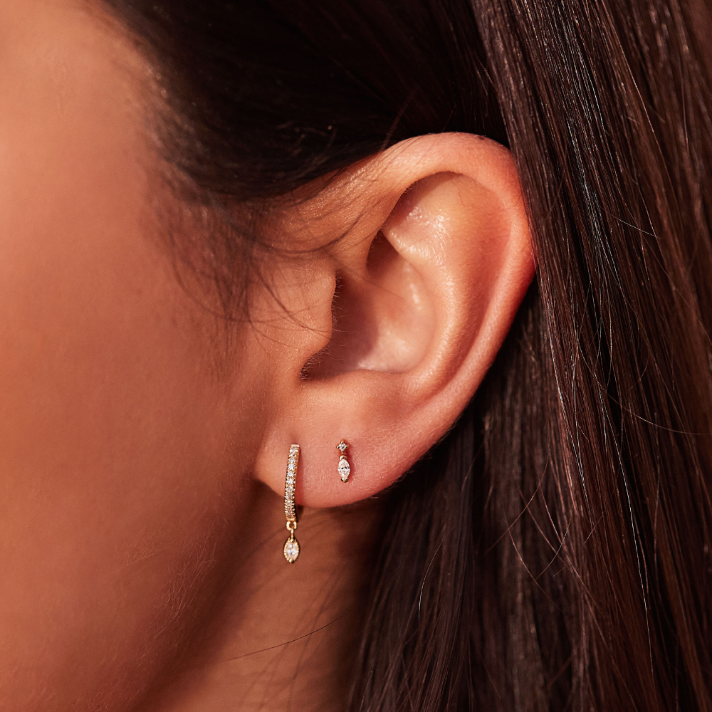 Gold marquise diamond drop hoop earrings with gold marquise diamond stud earring in one ear lobe