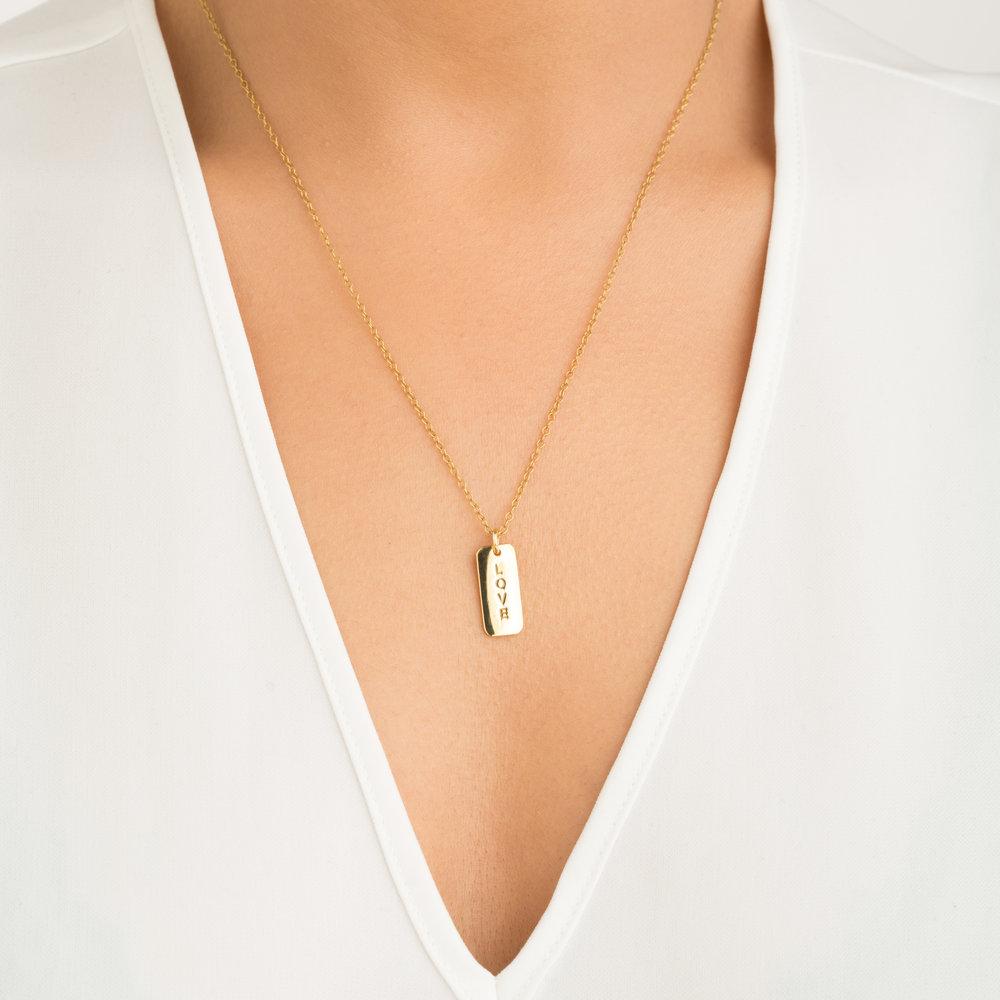 Gold personalised tag necklace with 'LOVE' engraved on it around a neck of a woman wearing a v neck top