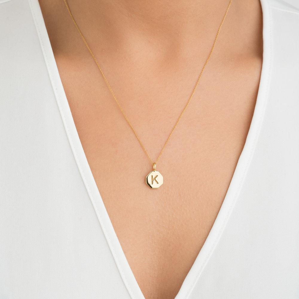 Gold personalised hexagon necklace with the letter 'K' engraved on it around a neck with a white v neck top