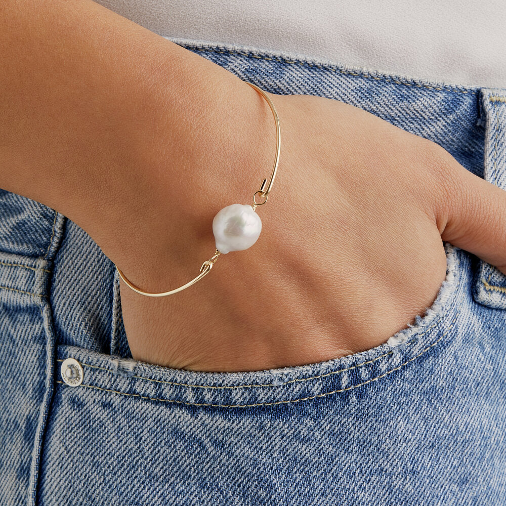 Baroque gold bangle with pearl on wrist with hand in jean pocket