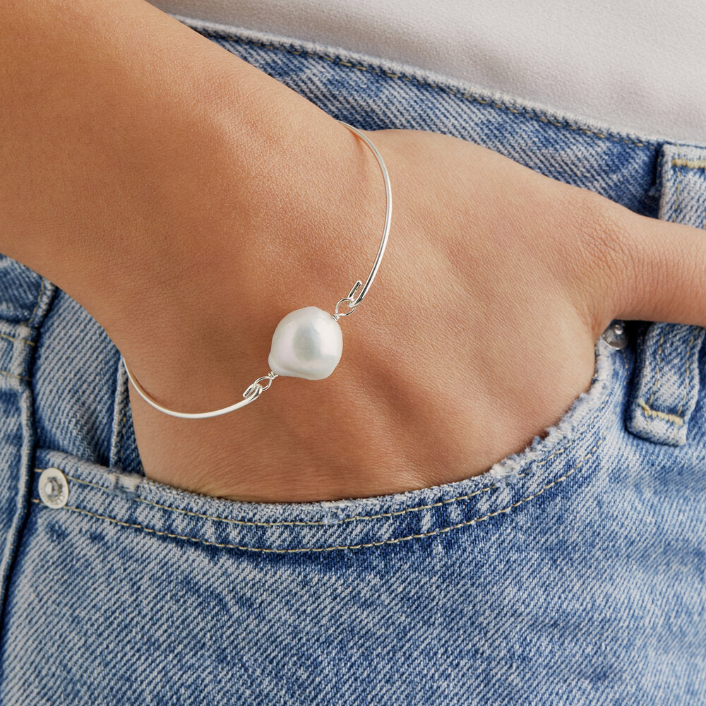 Silver baroque pearl bangle around a wrsit with hands in a denim pocket