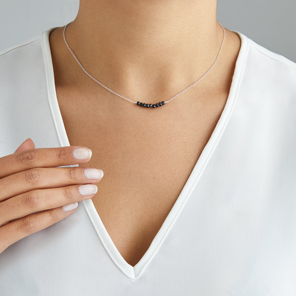 Silver spinel gemstone cluster choker around the neck of a woman wearing a white V neck top