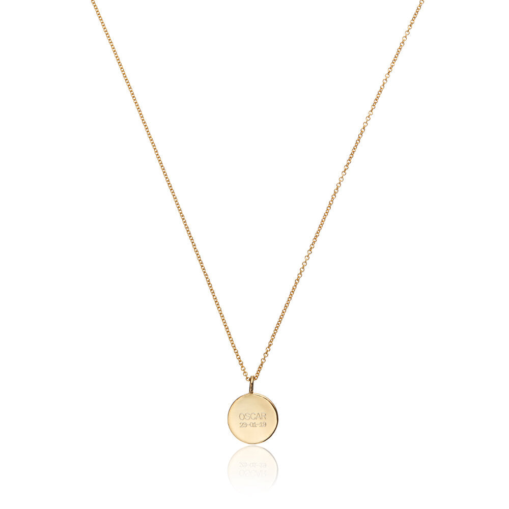 Distant shot of gold small diamond style disc necklace with 'OSCAR 23-01-19' engraved on it on a white background