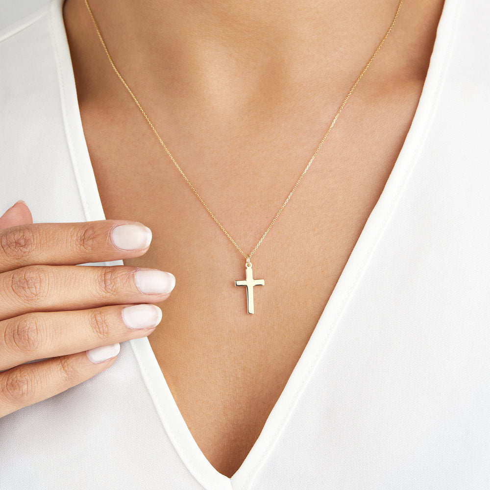 Solid gold cross necklace around the neck of a woman wearing a white V-neck top