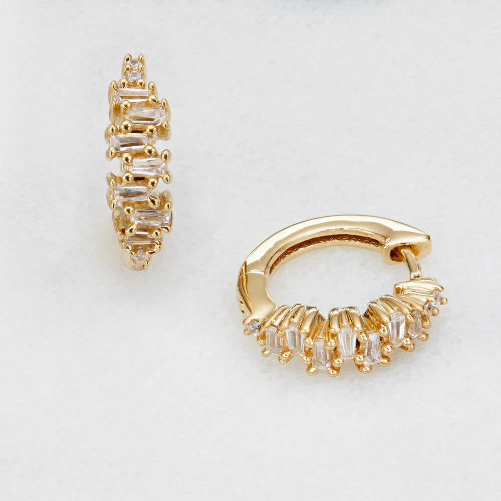 Gold diamond style stacked baguette huggie hoop earrings on a white surface