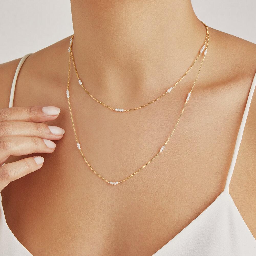 Gold layered mini pearl necklace around a neck with a white top