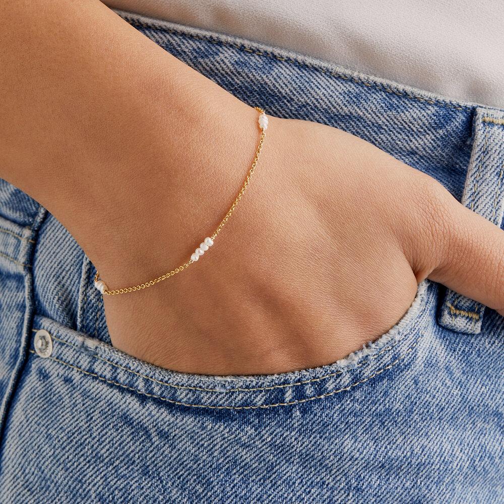 Gold mini pearl bracelet on a wrist with hand in blue jean pocket