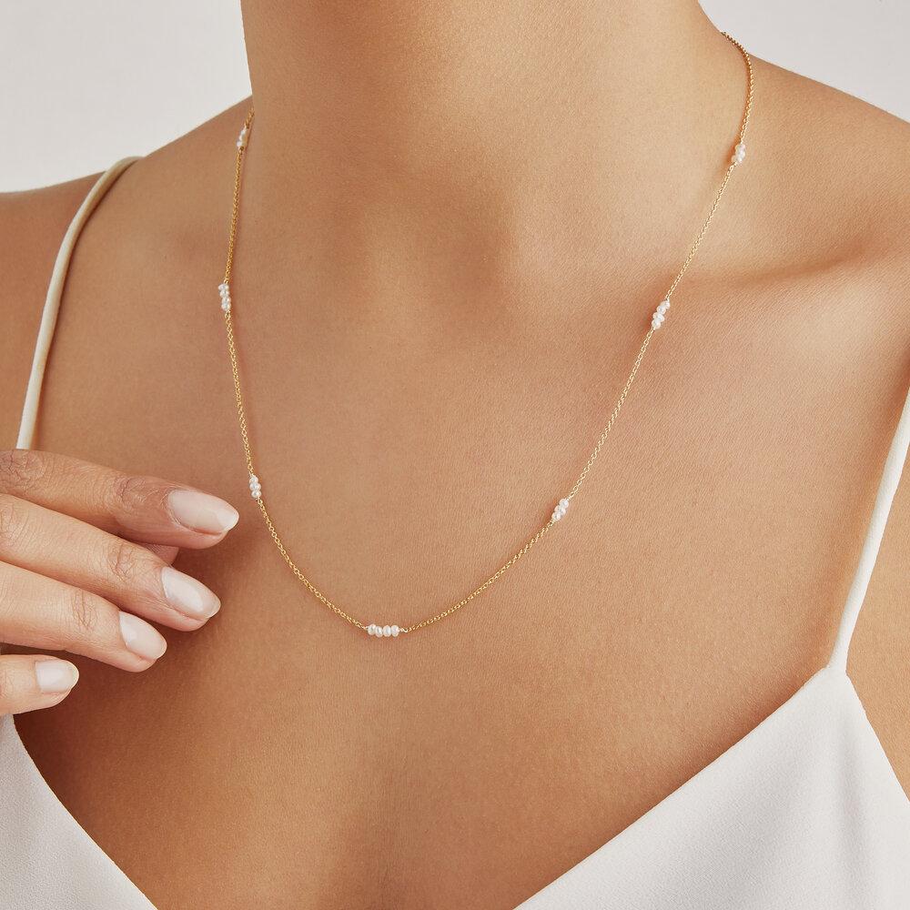 Gold mini pearl necklace around a neck with a white top
