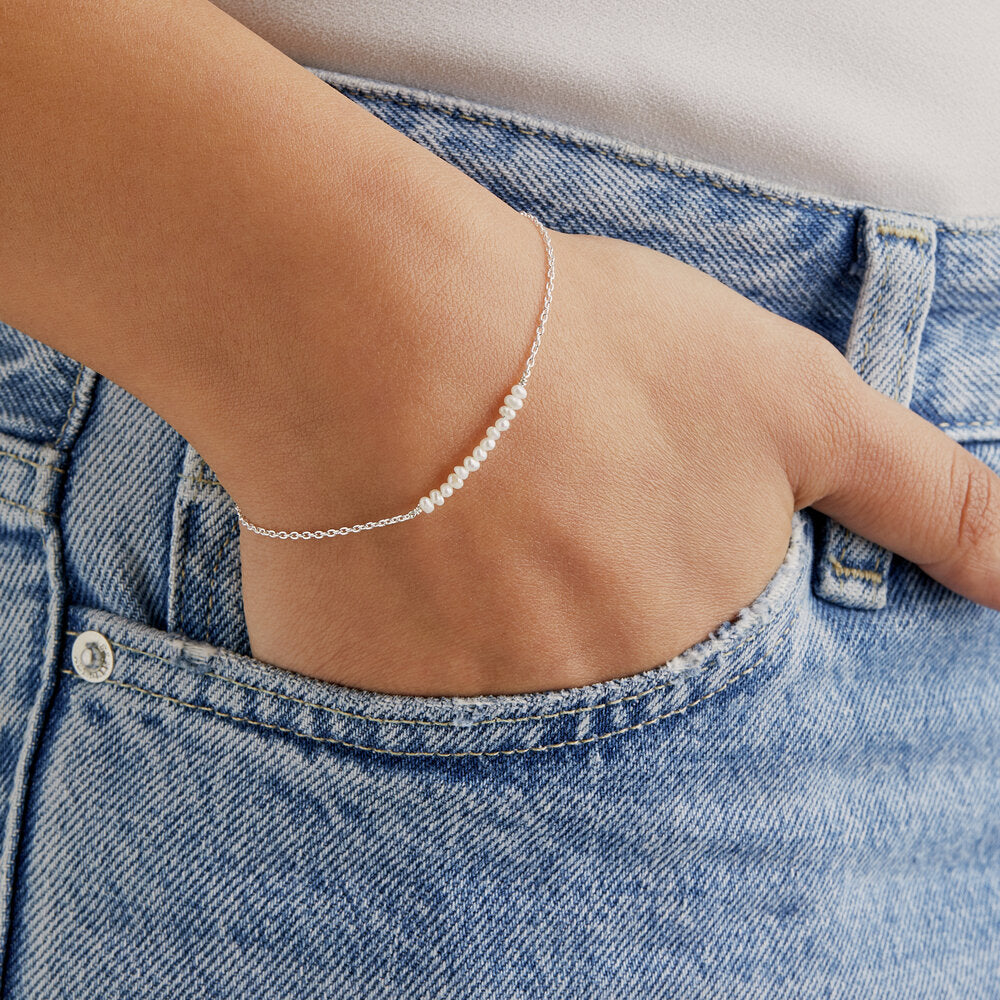 Silver small pearl cluster bracelet on a wrist with the hand in a blue denim pocket