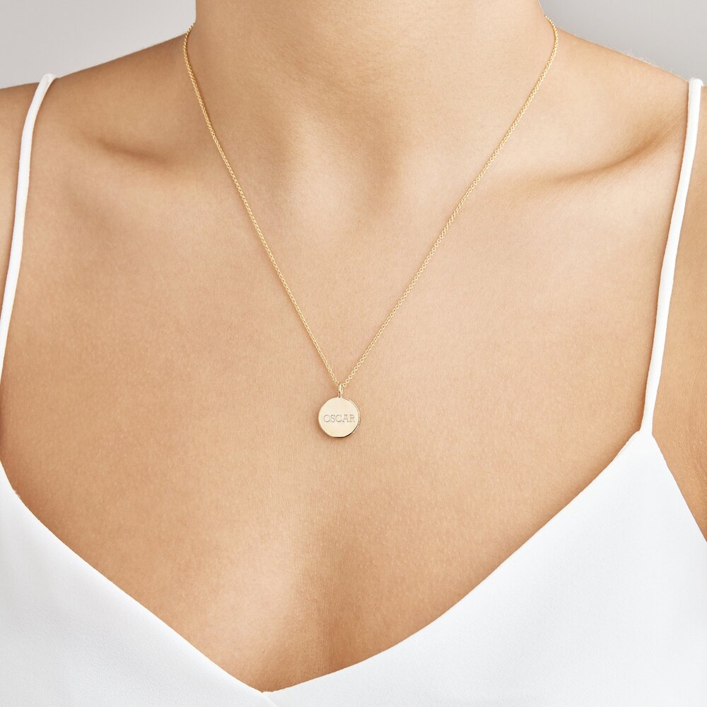 Gold small diamond style disc necklace with 'OSCAR' engraved on it around a neck