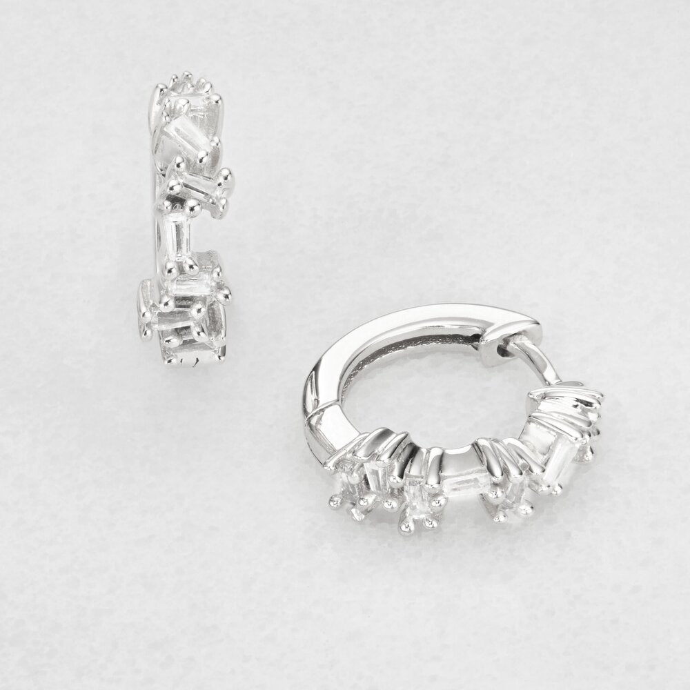 Silver diamond style jagged huggie hoop earrings on a marble surface
