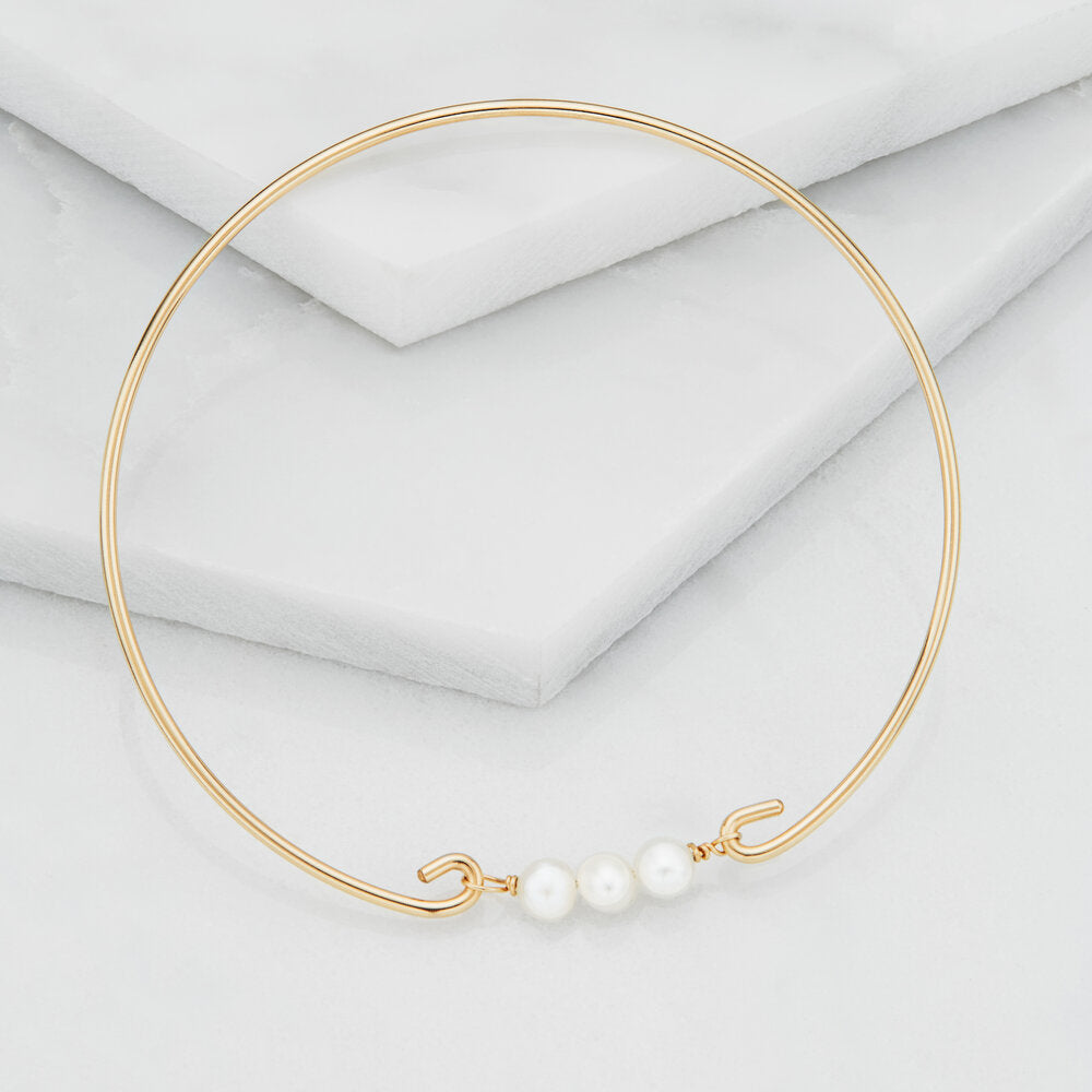 Gold cluster pearl bangle leaning on three marble blocks