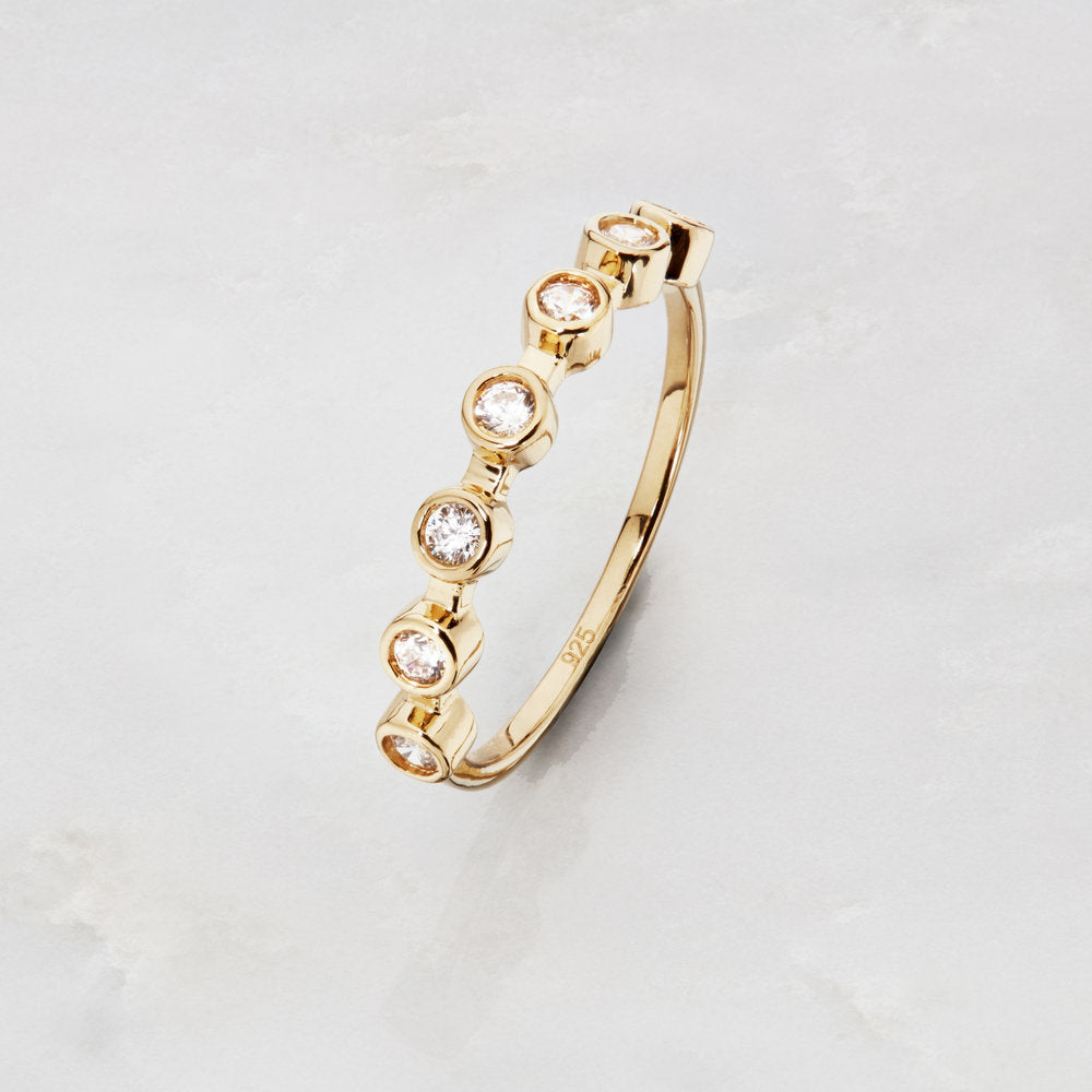Gold diamond style round eternity ring on a marble surface with the numbers '025' engraved