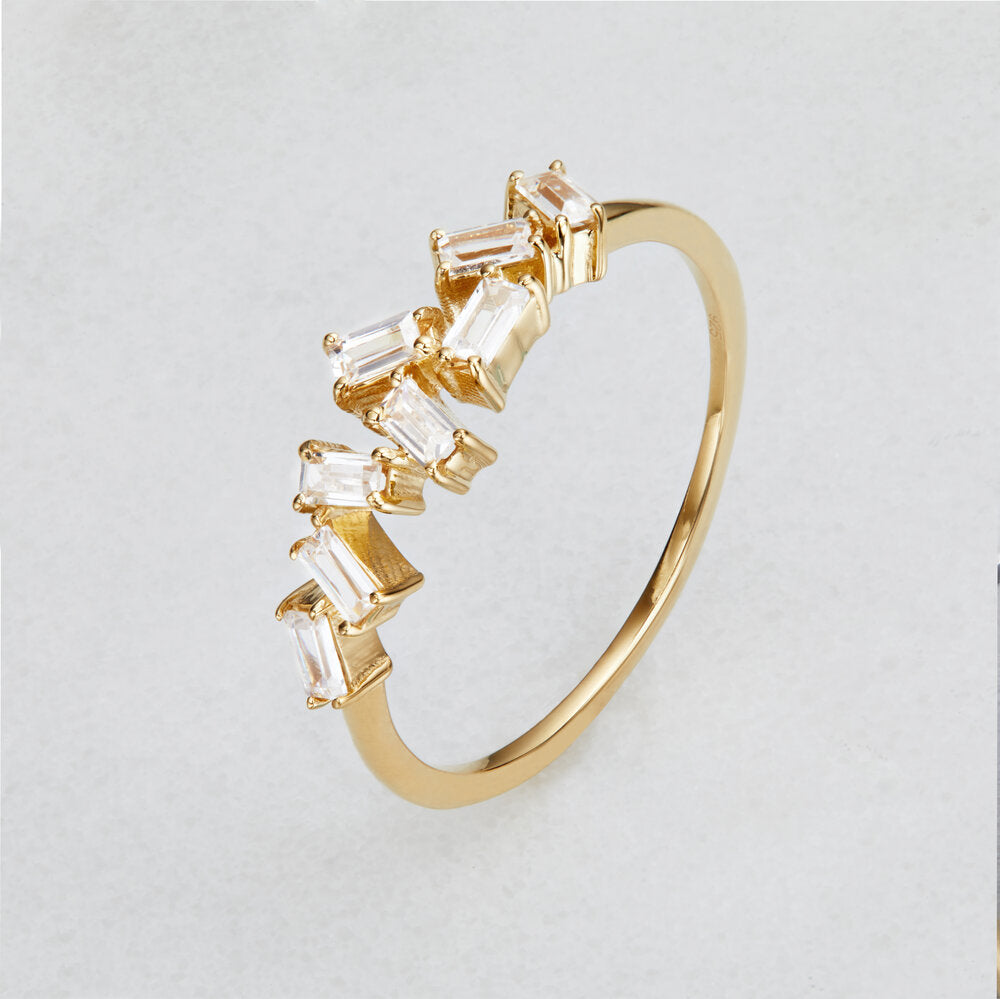 A gold diamond style baguette ring on a white surface from a side angle