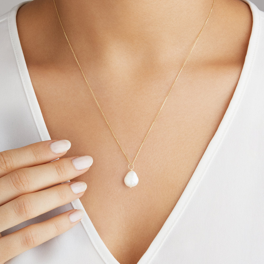 Gold large single pearl necklace around neck with a white v neck top