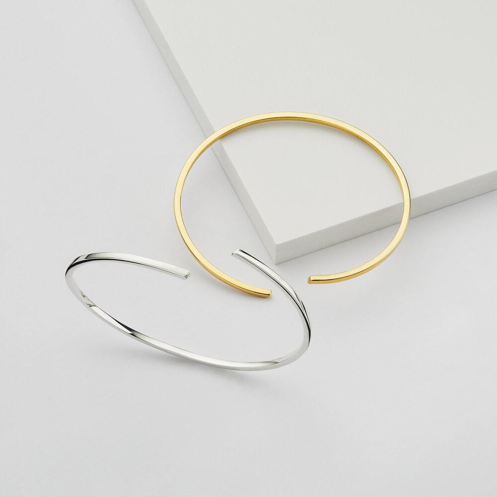 Silver thin spiral bangle and gold thin spiral bangle on marble surfaces