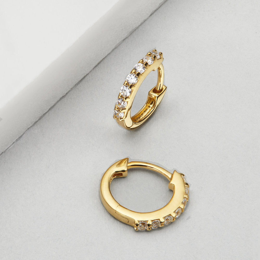 Gold diamond style huggie hoop earrings on a marble surface
