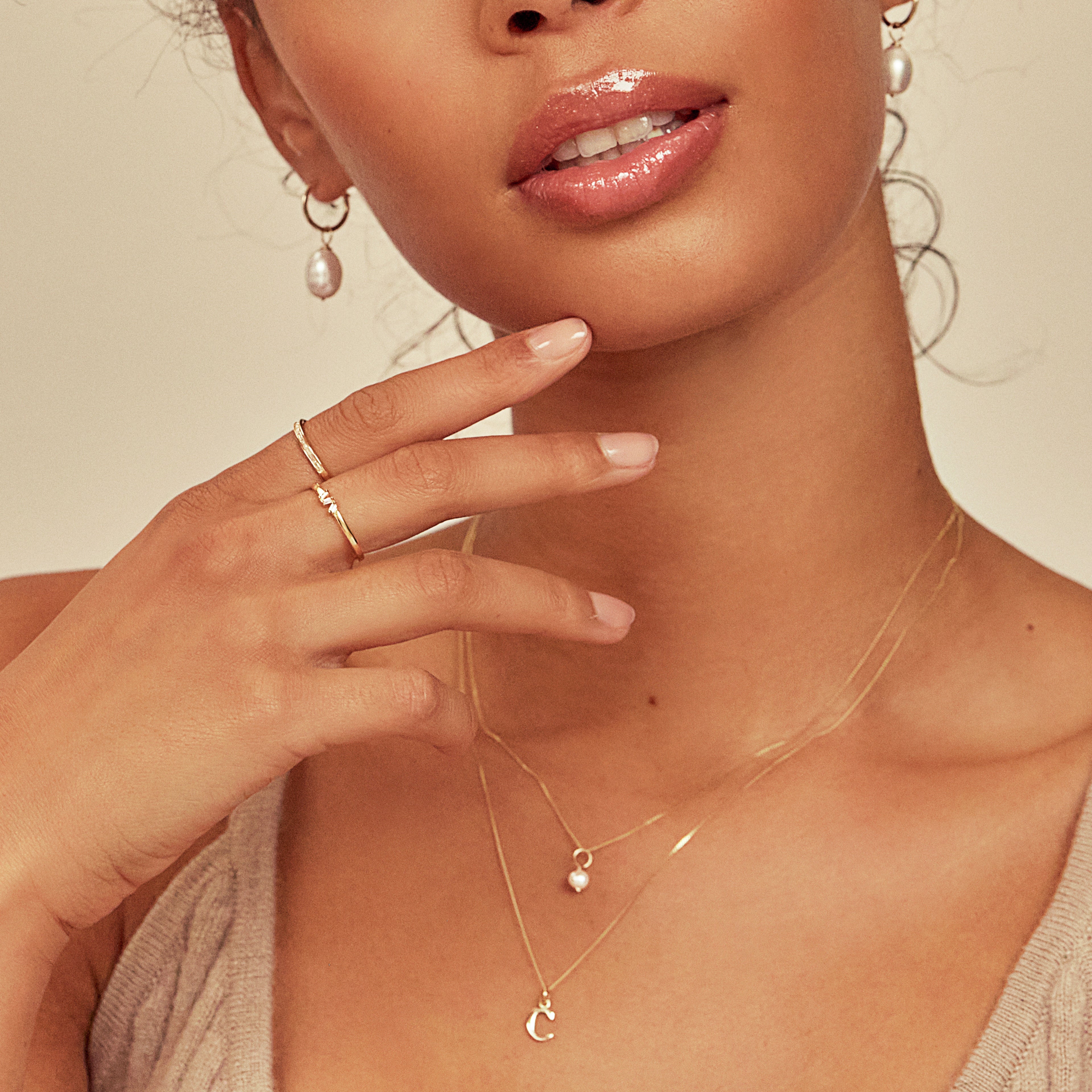 Gold diamond style three baguette ring on one finger, with gold diamond style baguette ring on another finger of a woman wearing pearl drop earrings, a pearl neckalce and a C letter necklace